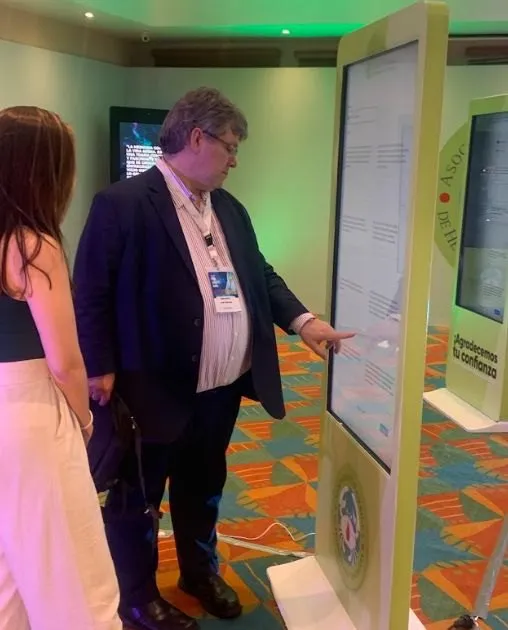 Dos asistentes frente a un póster digital en un tótem táctil